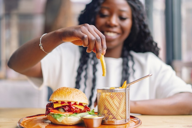 Junge Frau mit Afro-Haar, die einen leckeren klassischen Burger mit Pommes frites isst