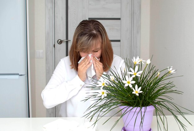 Foto junge frau mit allergien, gesichtstuch halten und niesen, blumen im vordergrund. ein mädchen mit allergien.