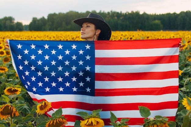 Junge Frau mit amerikanischer Flagge im Sonnenblumenfeld. 4. Juli Unabhängigkeitstag USA Konzept.