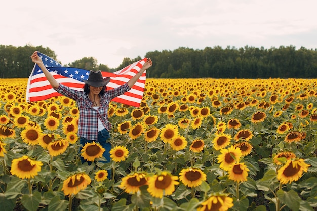 Junge frau mit amerikanischer flagge im sonnenblumenfeld th des juli-unabhängigkeitstag usa kopienraum