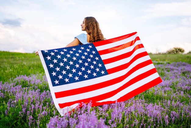 Junge Frau mit amerikanischer USA-Flagge auf blühender Wiese, Unabhängigkeitstag, 4. Juli