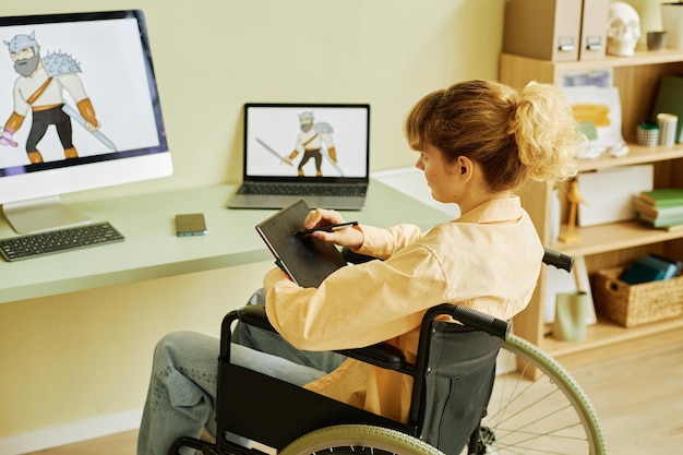 Junge Frau mit Behinderung sitzt im Rollstuhl vor Computern und zeichnet neue digitale Bilder
