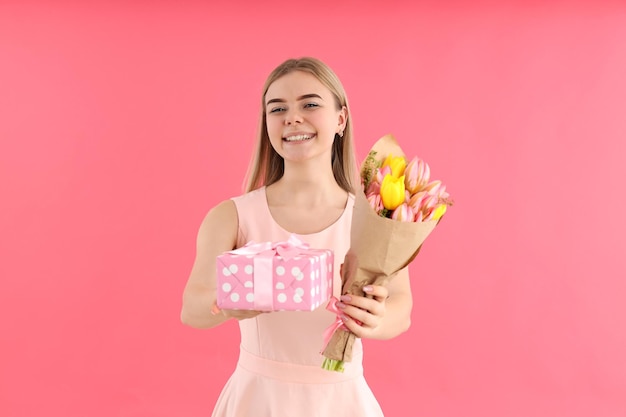 Junge Frau mit Blumenstrauß und Geschenkbox auf rosa Hintergrund