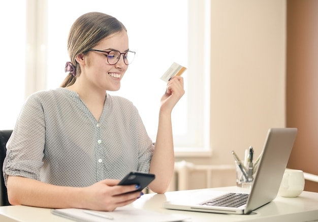 Junge Frau mit Brille, Arbeiten von zu Hause mit Smartphone und Computer, Frauenhände mit Smartphone