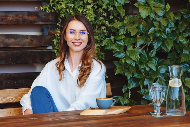 Junge Frau mit Brille sitzt an einem Tisch in einem Café