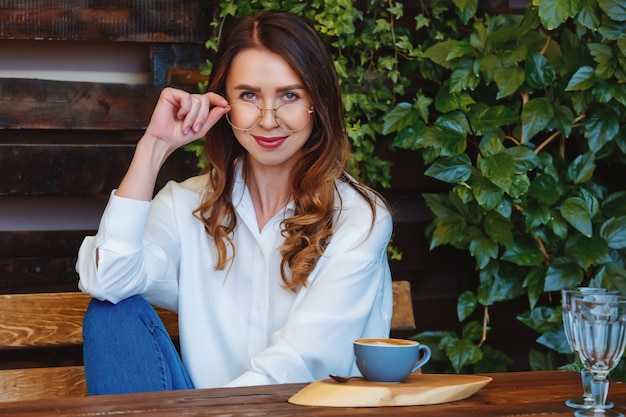 Junge Frau mit Brille sitzt an einem Tisch in einem Café