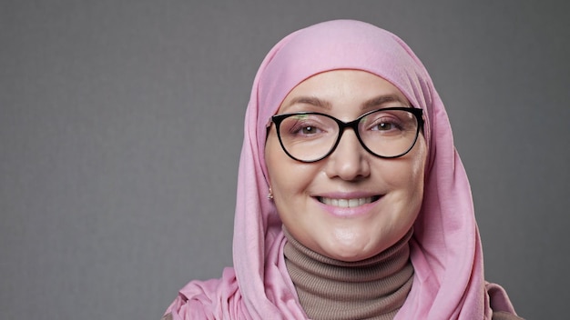 Junge Frau mit Brille und Hijab lächelt und schaut in die Kamera