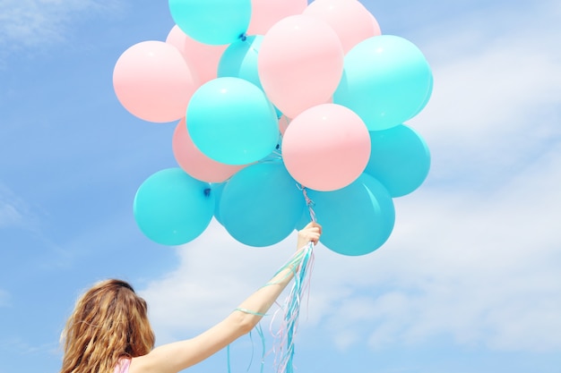 Junge Frau mit bunten Luftballons gegen blauen Himmel