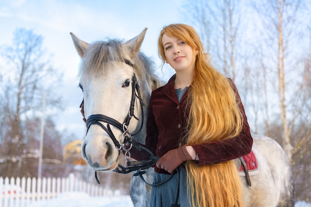 Junge Frau mit dem langen Haar mit Pferd im Winter