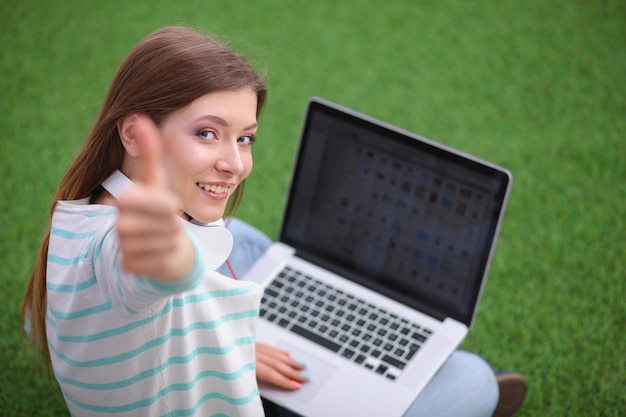 Foto junge frau mit dem laptop, der auf grünem gras sitzt junge frau portreit