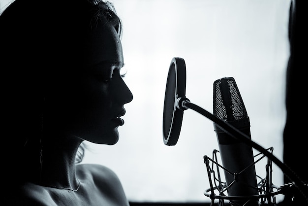 Junge Frau mit dem Mikrofon im Tonstudio Professionelle Gesangsaufnahme Schwarz-Weiß-Fotosession Schöne Sängerin Portrait Closeup