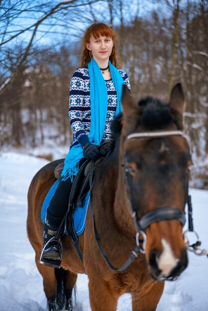 Junge Frau mit dem roten Haar auf einem Pferd im Winter