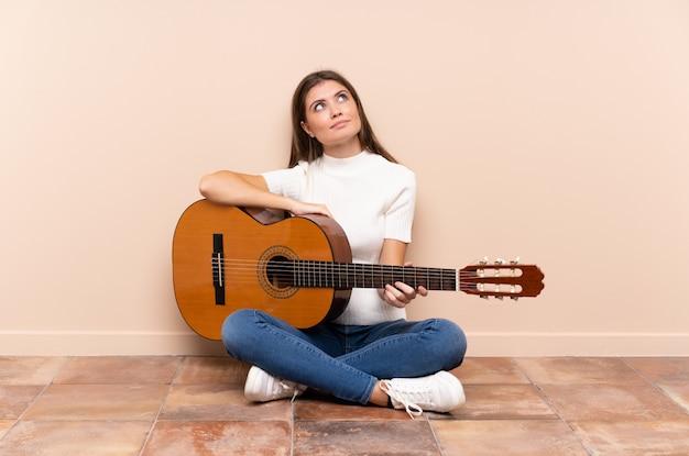 Junge Frau mit der Gitarre, die auf dem Boden oben lacht und schaut sitzt