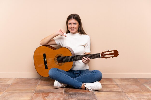 Junge Frau mit der Gitarre, die auf dem Boden stolz und selbstzufrieden sitzt