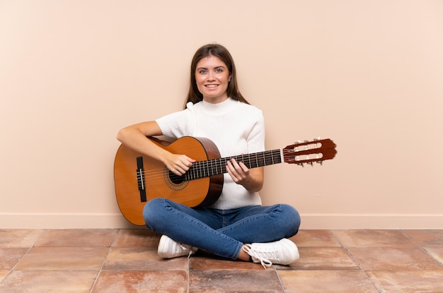 Junge Frau mit der Gitarre, die auf dem Bodenlachen sitzt