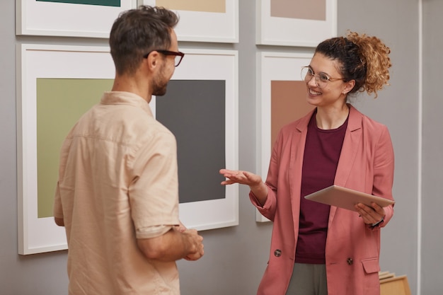 Junge Frau mit digitaler Tafel, die moderne Kunst mit Mann bespricht, den sie an der Kunstgalerie stehen