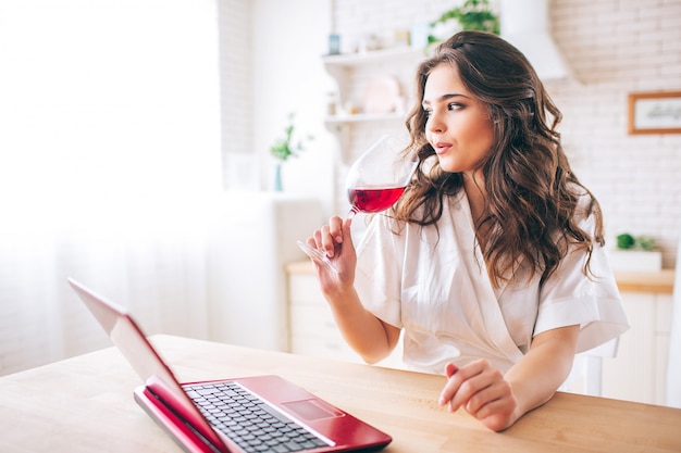 Junge Frau mit dunklem Haar, das in der Küche steht und Rotwein trinkt