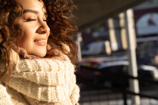 Junge Frau mit dunklem, lockigem Haar, Nahaufnahme, warm gekleideter Schal, Winterfrost, sonniger Tag auf der Straße in der Stadt.