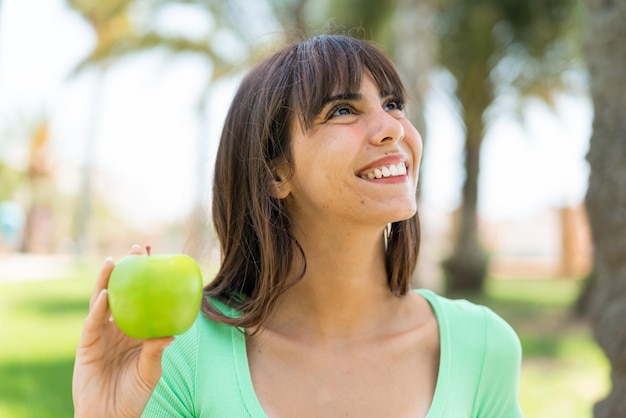 Junge Frau mit einem Apfel im Freien, die lächelnd nach oben schaut