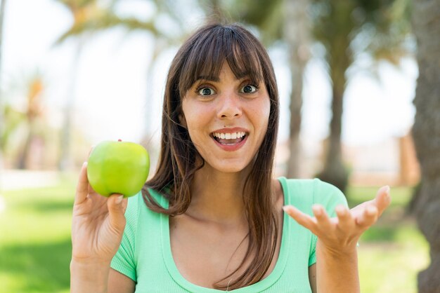 Junge Frau mit einem Apfel im Freien mit schockiertem Gesichtsausdruck