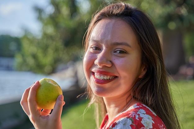 Junge Frau mit einem Apfel in der Hand Frau mit perfekten weißen Zähnen lächelt in die Kamera