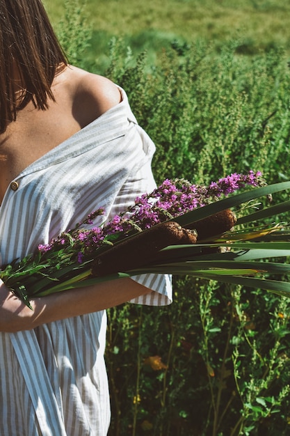 Junge Frau mit einem Blumenstrauß der wilden Blumen, die in einem Garten entspannen