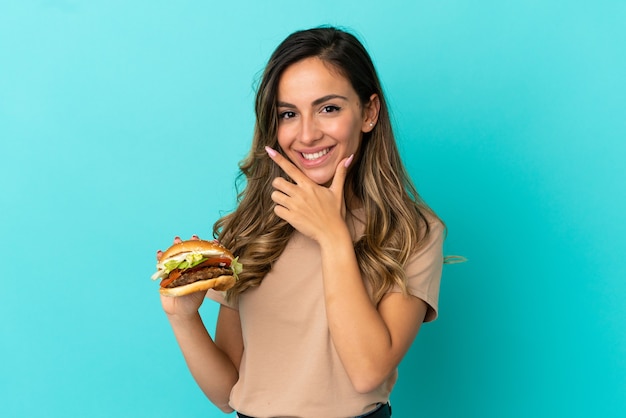 Junge Frau mit einem Burger über isoliertem Hintergrund glücklich und lächelnd happy