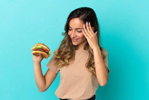 Junge Frau mit einem Burger über isoliertem Hintergrund lachen holding