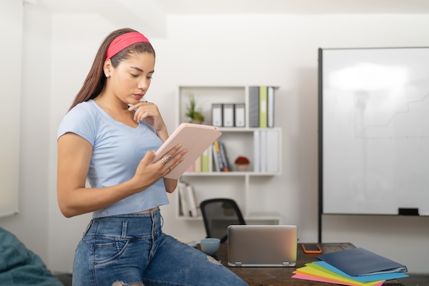 Junge Frau mit einem digitalen Tablet, das sich auf den Schreibtisch stützt