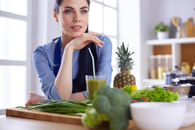 Junge Frau mit einem Glas leckeren, gesunden Smoothie am Tisch in der Küche