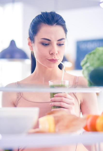 Junge Frau mit einem Glas leckeren, gesunden Smoothie am Tisch in der Küche