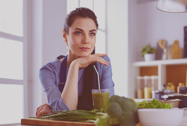 Junge Frau mit einem Glas leckeren, gesunden Smoothie am Tisch in der Küche