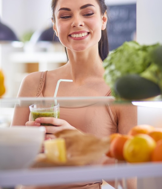 Junge Frau mit einem Glas leckeren, gesunden Smoothie am Tisch in der Küche