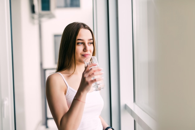 Junge Frau mit einem Glas Wasser, das auf Sofa im Raum sitzt