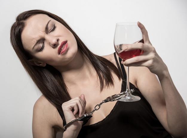 Junge Frau mit einem Glas Wein und Handschellen.