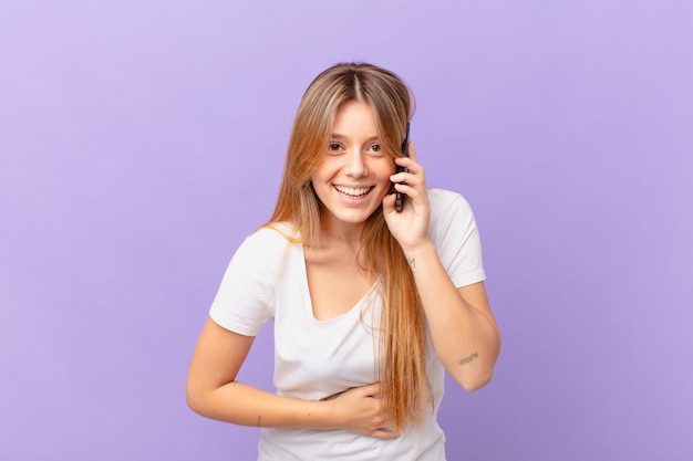 Junge Frau mit einem Handy, die laut über einen lustigen Witz lacht