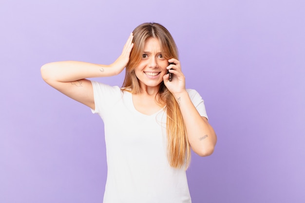 Junge Frau mit einem Handy, die sich gestresst, ängstlich oder ängstlich fühlt, mit den Händen auf dem Kopf