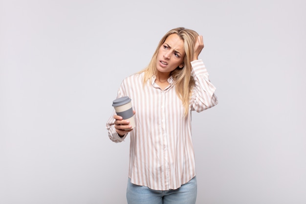 Junge Frau mit einem Kaffee, der sich verwirrt und verwirrt fühlt, sich am Kopf kratzt und zur Seite schaut