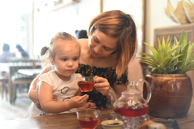 Junge Frau mit einem kleinen Mädchen, das Tee aus einer Teekanne in einem Café trinkt
