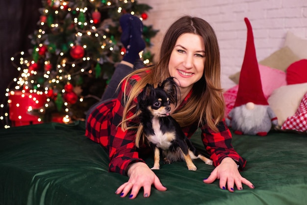 junge frau mit einem kleinen schwarzen hund in ihren armen nahe dem weihnachtsbaum zu weihnachten zu hause