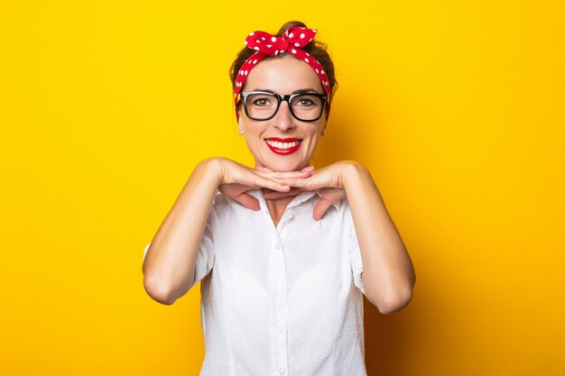 Junge Frau mit einem Lächeln, Brille und einem roten Stirnband auf dem Kopf an einer gelben Wand tragend.