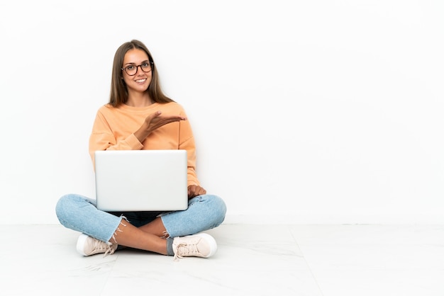 Junge Frau mit einem Laptop auf dem Boden, die eine Idee präsentiert und dabei lächelnd in Richtung blickt