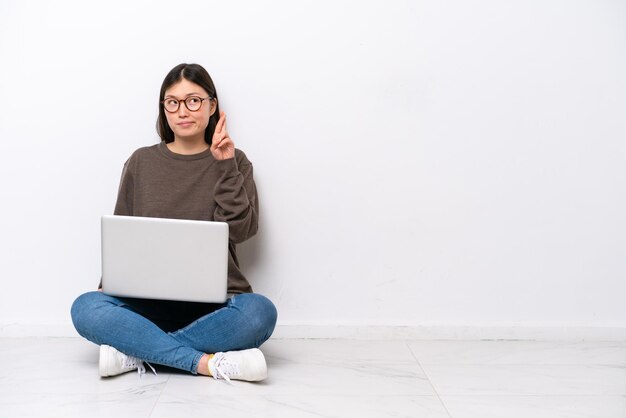 Junge Frau mit einem Laptop auf dem Boden sitzend, die Finger kreuzen und das Beste wünschen