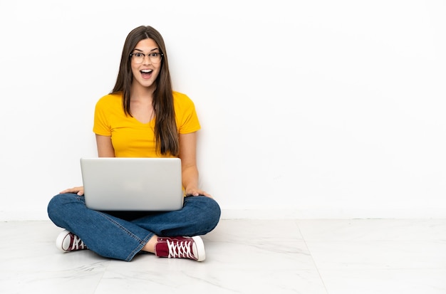 Junge Frau mit einem Laptop auf dem Boden sitzend mit überraschtem Gesichtsausdruck