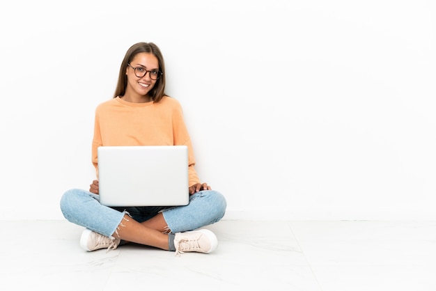 Junge Frau mit einem Laptop auf dem Boden sitzend und lachen