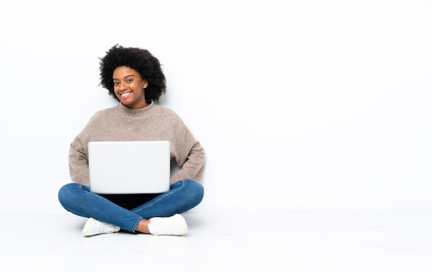 Junge Frau mit einem Laptop, der auf dem Boden lachend sitzt