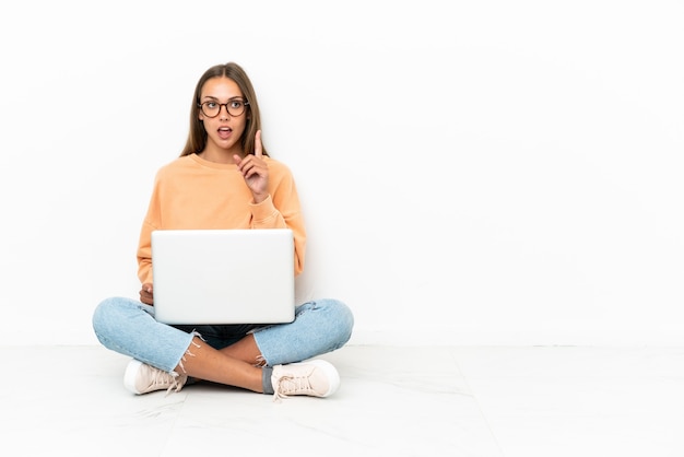 Junge Frau mit einem Laptop, der auf dem Boden sitzt und eine Idee denkt, die mit dem Finger nach oben zeigt