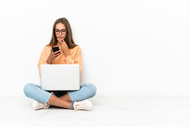 Junge Frau mit einem Laptop, der auf dem Boden sitzt und eine Nachricht denkt und sendet