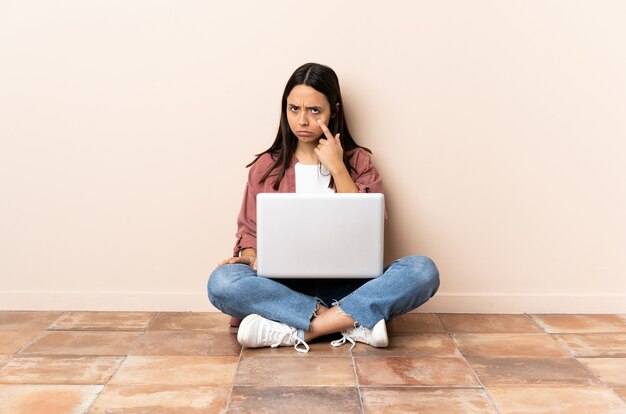 Junge Frau mit einem Laptop, der auf dem Boden sitzt und etwas zeigt