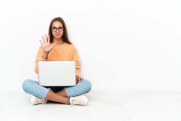 Junge Frau mit einem Laptop, der auf dem Boden sitzt und mit den Fingern fünf zählt